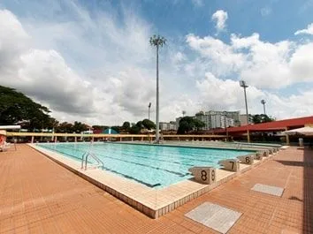 Outdoor lap pool with lane ropes and floodlights under a cloudy sky