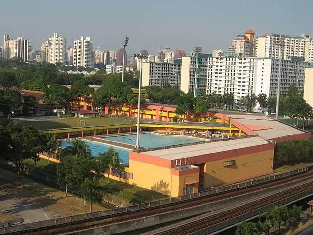 Aerial view of a public swimming complex beside an MRT line and HDB flats in Singapore